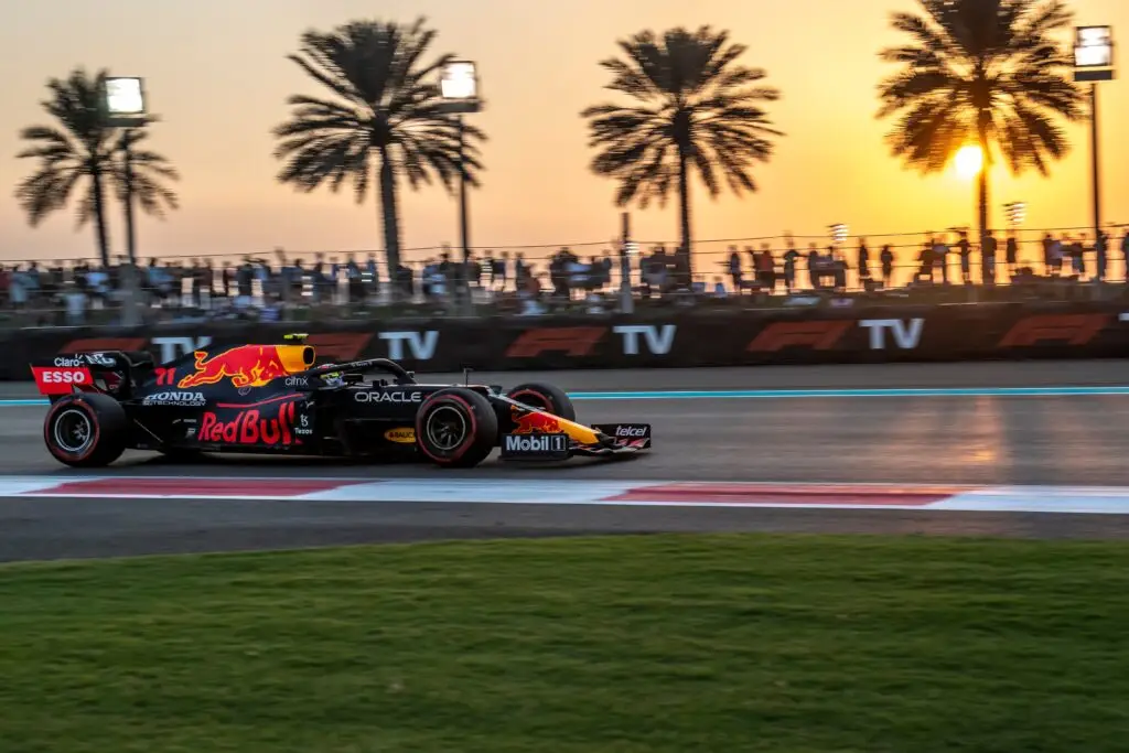 Red Bull Formula 1 car racing past palm trees at sunset at Yas Marina Circuit.