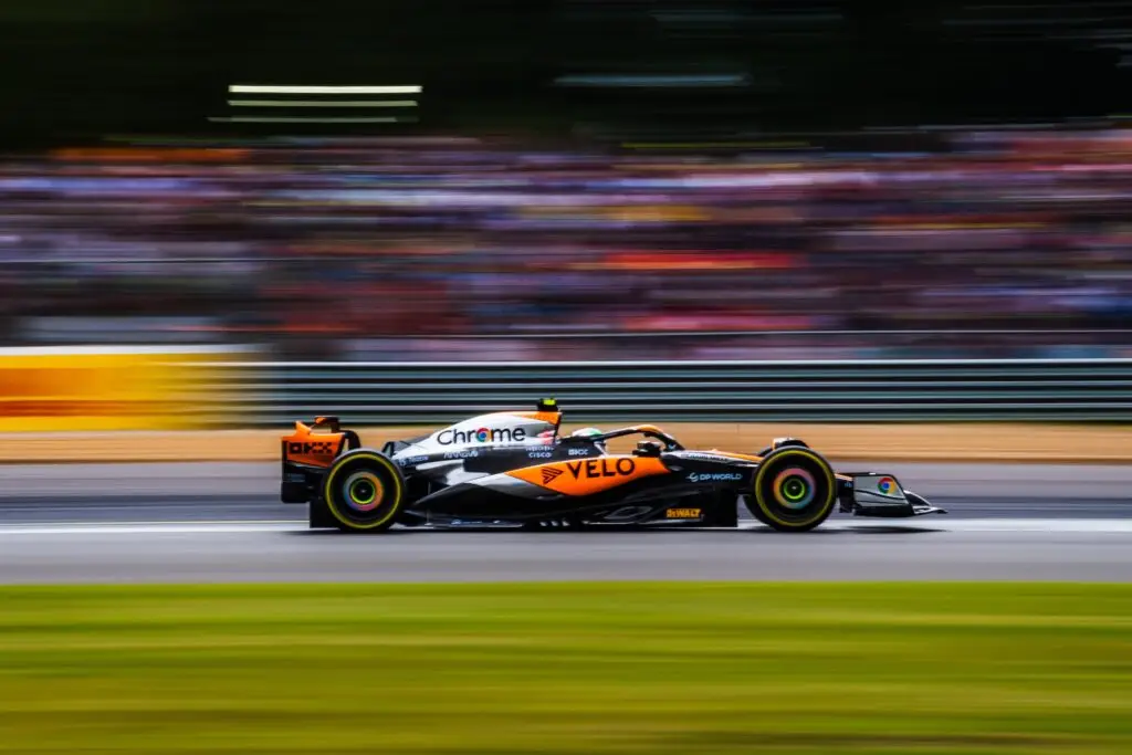 McLaren Formula 1 car speeding past blurred grandstands at the British Grand Prix.