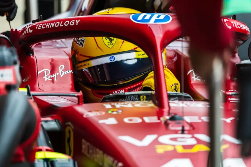 Close-up of a Ferrari driver wearing a yellow helmet inside the cockpit.