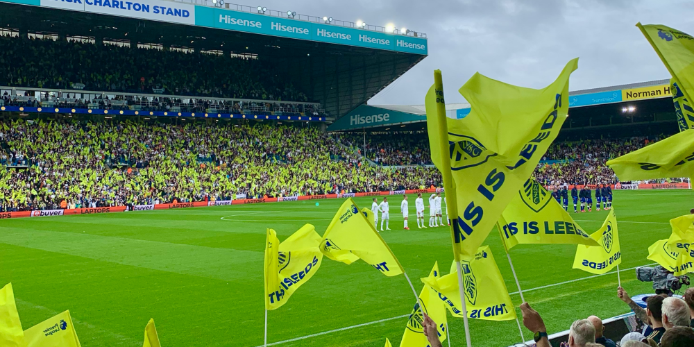 Packed stands at Elland Road with Leeds United supporters waving flags.