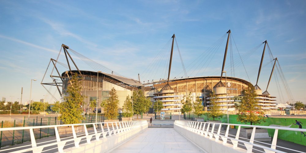 View of the bridge leading to Etihad Stadium under a clear blue sky.
